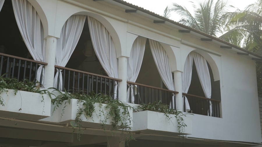 A white building facade featuring arched openings, hanging curtains, and a balcony at Bougainvillea, Alibaug.