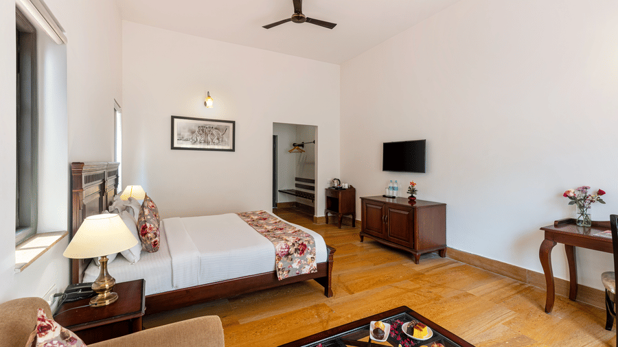Corner view of the Superior Room at The Hunting Lodge, Udaipur, featuring a double bed and a TV table in front of it in a spacious room.