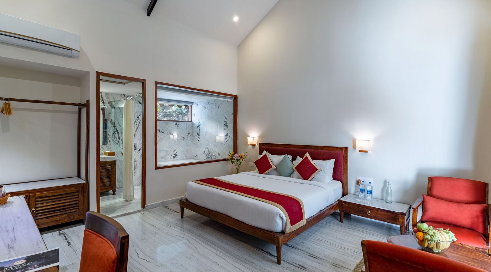 full view image of the luxury bathtub villas featuring a king size bed in the centre of the room and a family seating area with red cushioned chairs at aranya vilas in udaipur