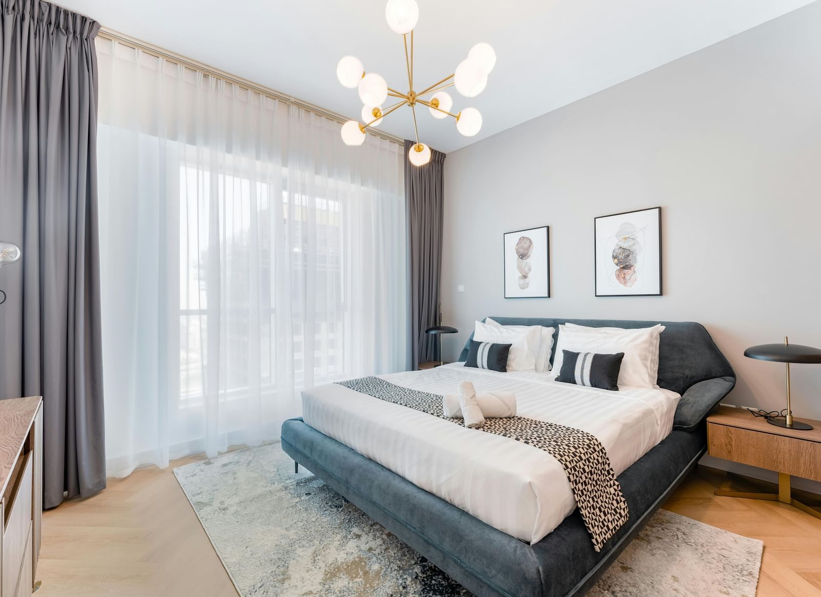 A room featuring a large bed, chandelier, spacious window, and stylish furnishings
