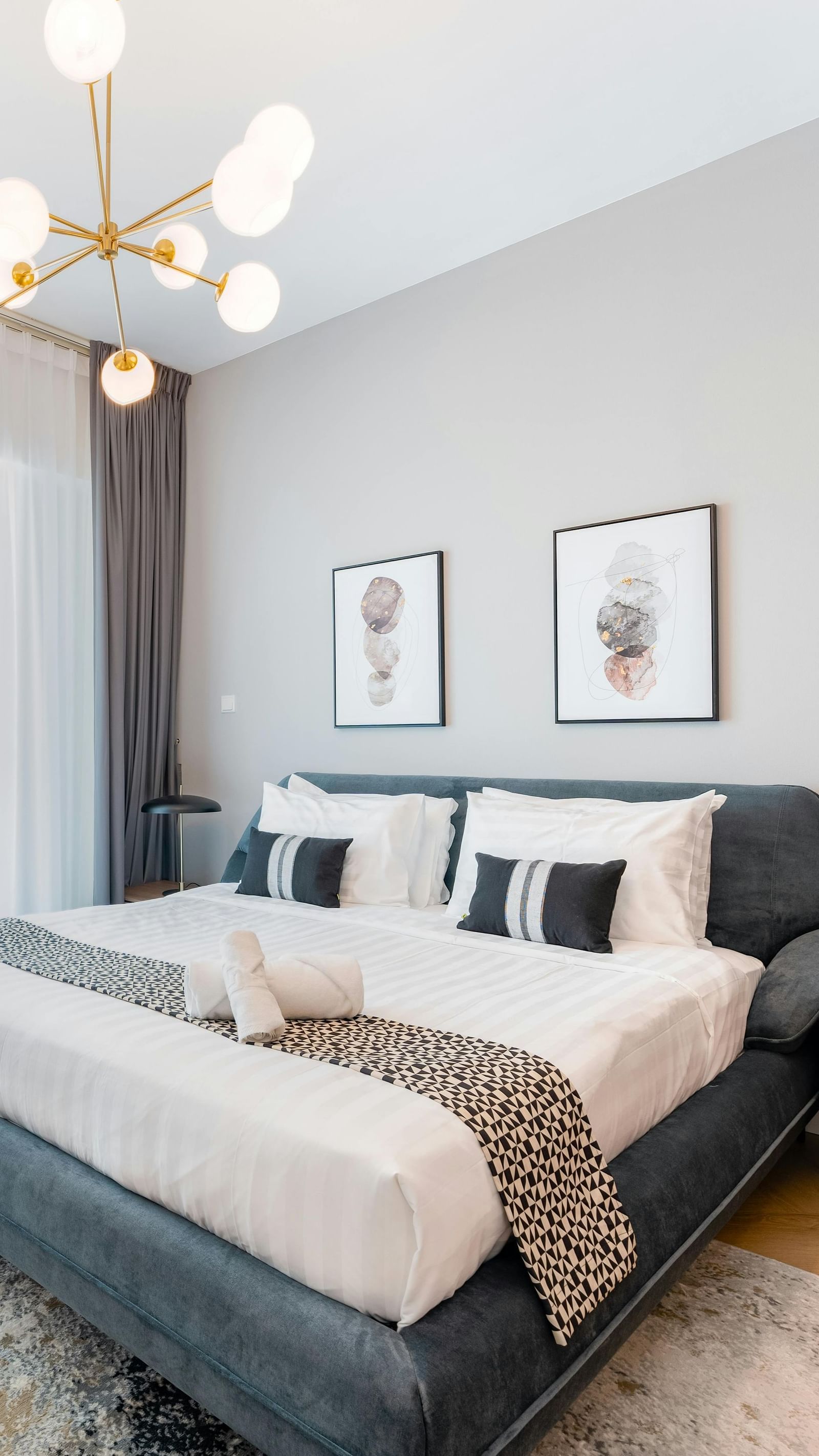 A room featuring a large bed, chandelier, spacious window, and stylish furnishings
