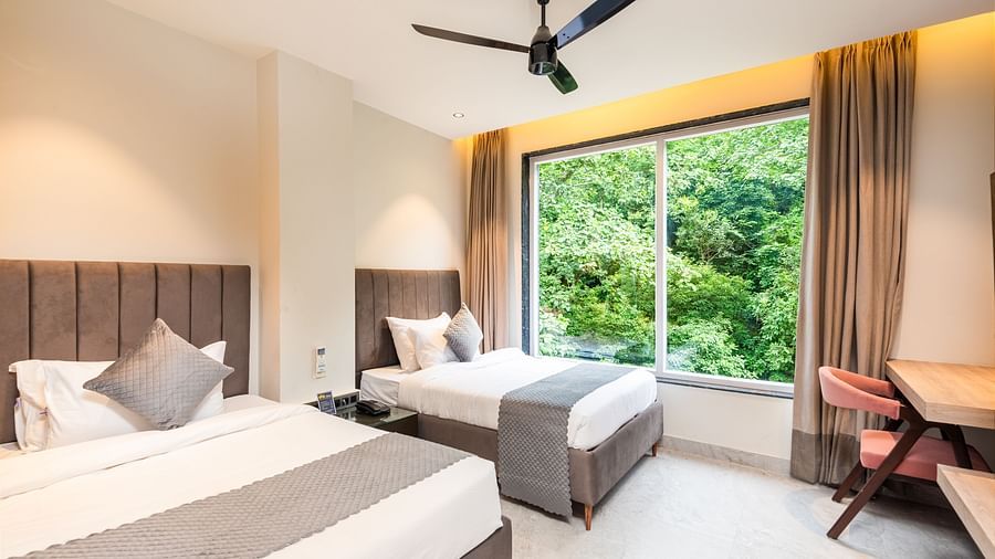 Deluxe Room at DLS Divine River Resort and  Spa featuring a two king bed , side table, warm lighting and a balcony with forest views.