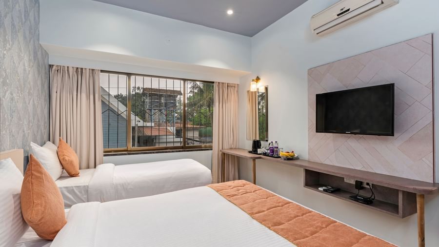 Bright, airy room at Emerald Retreat, Tungarli with a double bed & a single bed, a TV unit, and pastel-themed decor for a restful stay.