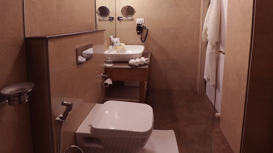 Bathroom with a white toilet, a sink, and a shower area, with a towel hanging nearby -Hotel Denzong Shangrila Lords Inn