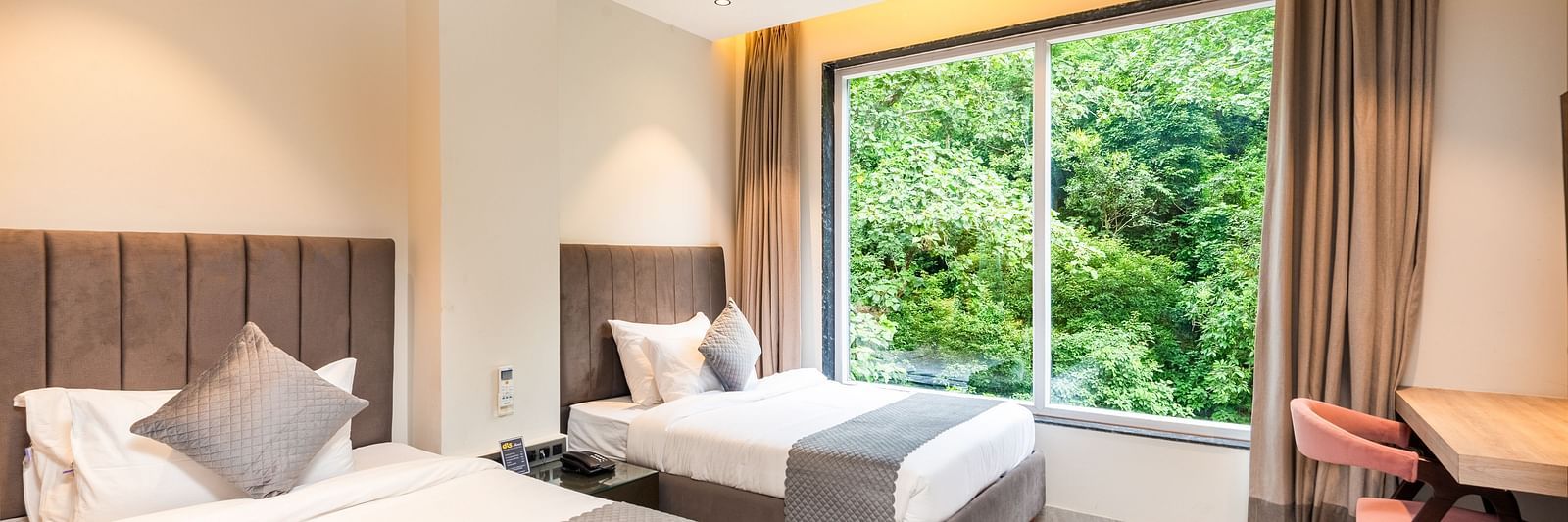 Deluxe Room at DLS Divine River Resort and  Spa featuring a two king bed , side table, warm lighting and a balcony with forest views.