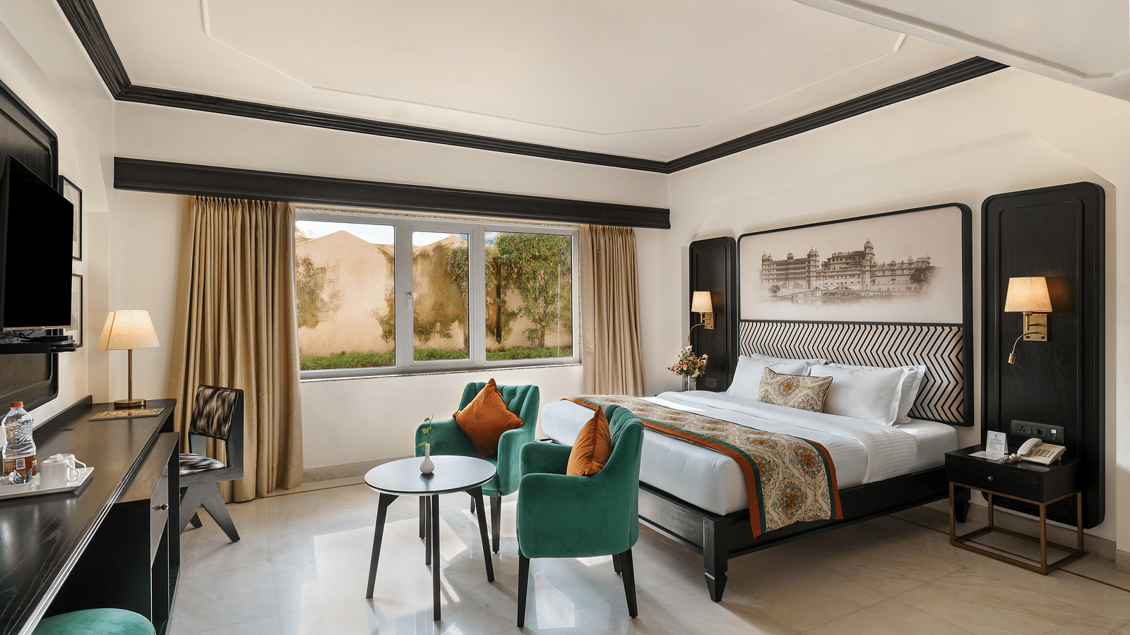 a spacious hotel  room in udaipur featuring a king size bed, two comfortable green chairs, a cabinet with a table lamp and a window overlooking the city - Hotel Rajdarshan, Udaipur.