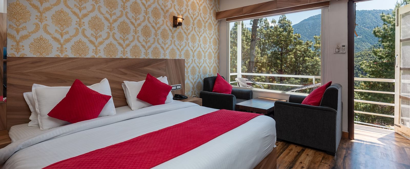  Elegant hotel room with a large bed featuring red and white bedding, stylish wallpaper, a cosy seating area, and a balcony with scenic mountain and forest views - DLS Nature Trinket Resort, Dalhousie.