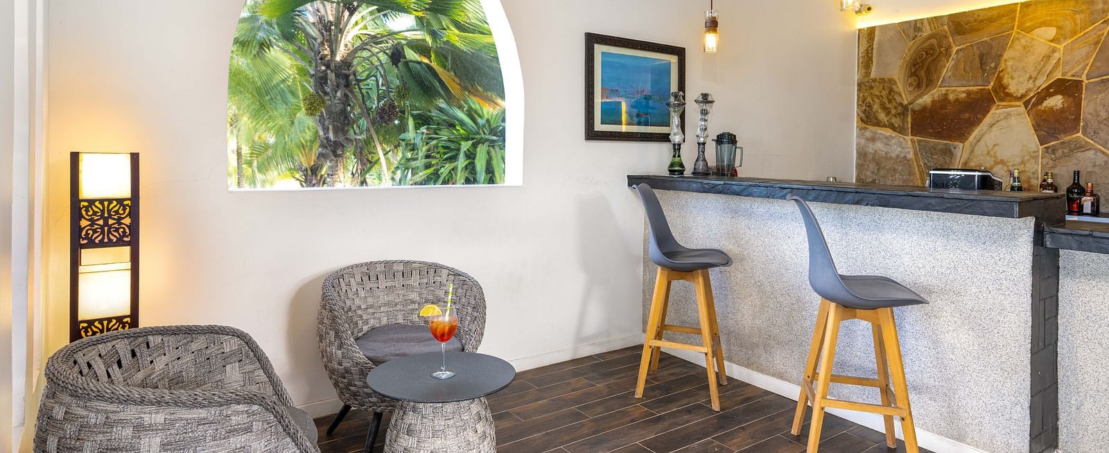 View of a relaxed bar corner with cushioned seating and an open archway overlooking greenery at shooting star Boutique Hotel