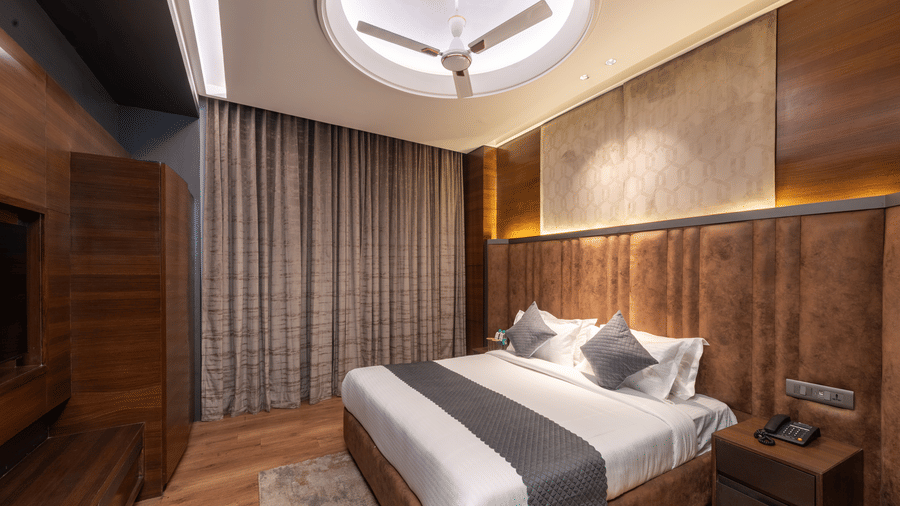A bedroom with a king size bed, side tables, ceiling fan, and wardrobe indoors at DLS Hotels Amritsar.