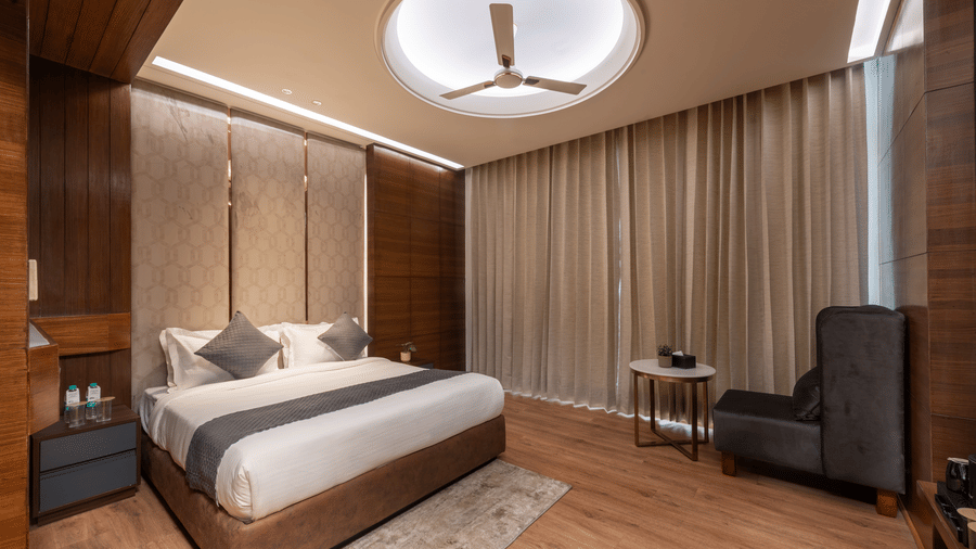 A bedroom with a king size bed, side tables, chair, and ceiling fan inside at DLS Hotels Amritsar.