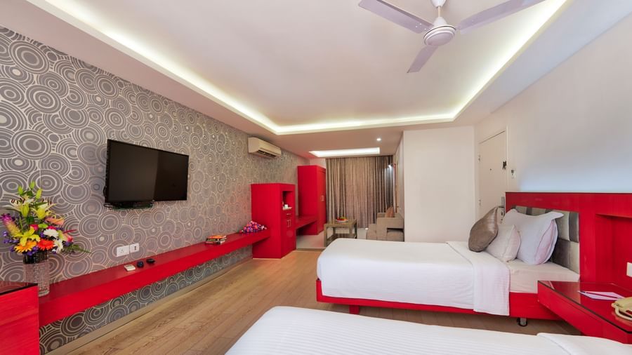 A hotel bedroom with a large white bed, red furniture accents, and a television on the wall | Grande Chalet | Grande Bay Resort & Spa, Mamallapuram