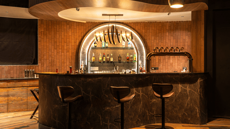 Rhythm & Brews equipped with high chairs and a variety of bottles displayed on shelves, illuminated by warm lighting at The Qualia Resort Club & Brewery, Udaipur.