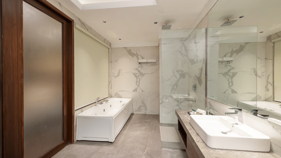 A bathroom with a bathtub, sink, mirror, and glass partition arranged indoors at DLS Hotels Amritsar.