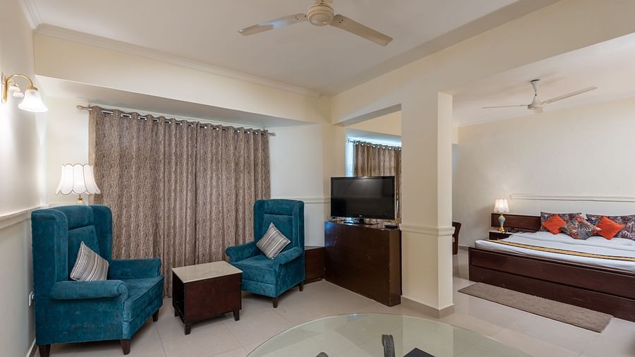 A wide angle shot of a room that features a king size bed, a television, two couched and a table | DLS The Pearl