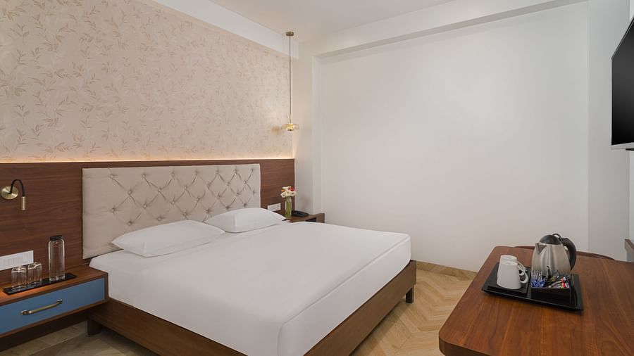Side view of a spacious room featuring a large bed with a cushioned headboard, wooden bedside tables on either side, and inviting lighting | Hotel Ganga Maiya