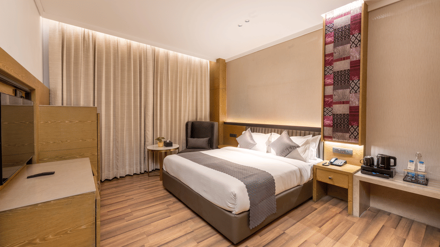 A bedroom with a king size bed, side tables, curtains, and wooden cabinets inside at DLS Hotels Amritsar.