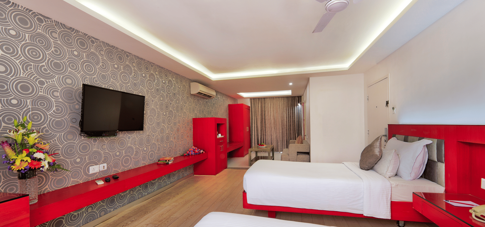 A hotel bedroom with a large white bed, red furniture accents, and a television on the wall - Grande Bay Resort & Spa, Mamallapuram