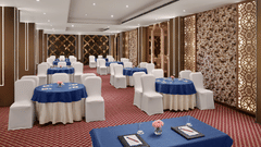An image of a banquet hall with chairs draped in white cloth and placed near round tables - Deventure Sarovar Portico, Patel Nagar