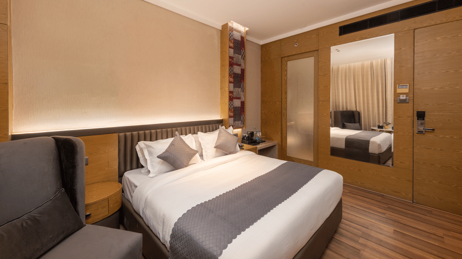 A rbedoom with a king size bed, chair, mirror, and wardrobe area visible inside at DLS Hotels Amritsar.