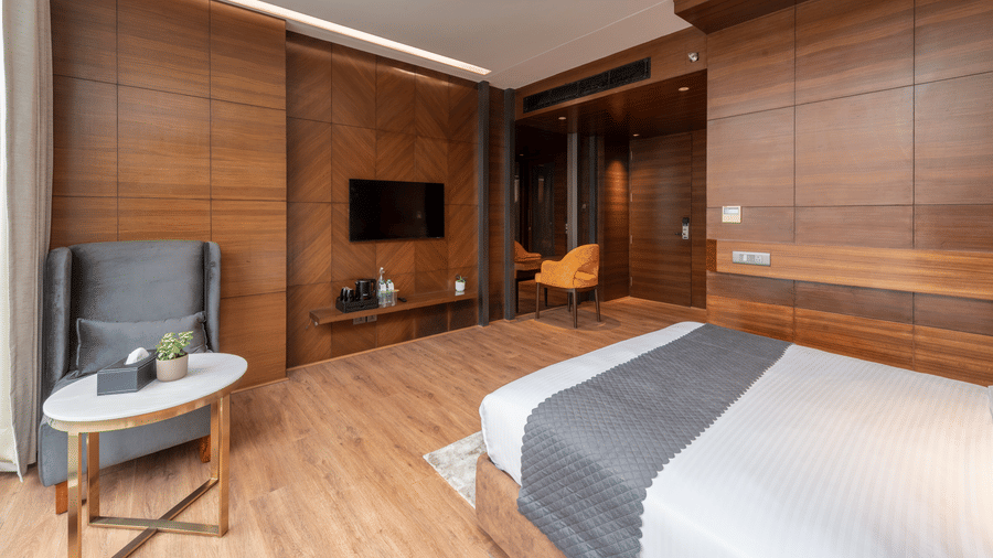 A bedroom with a king size bed, wall-mounted TV unit, chair, table, and work desk inside at DLS Hotels Amritsar.