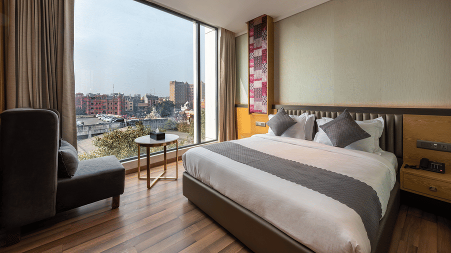 A bedroom with a king size bed, large window, armchair, curtains, and bedside tables at DLS Hotels Amritsar.