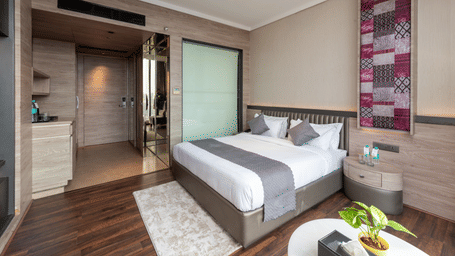 A bedroom with a king size bed, bedside tables, teapoy, wall paneling, doorway, and lighting fixtures at DLS Hotels Amritsar.