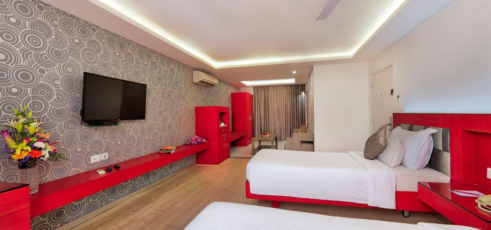 A hotel bedroom with a large white bed, red furniture accents, and a television on the wall | Grande Chalet | Grande Bay Resort & Spa, Mamallapuram