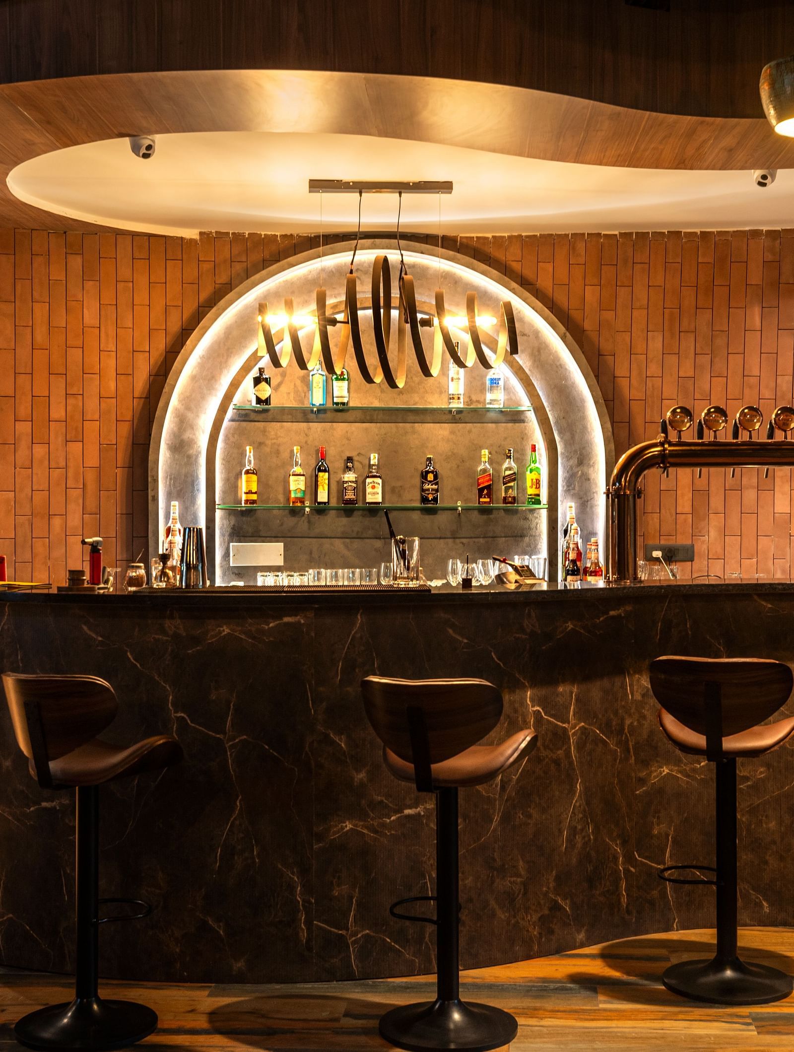 Rhythm & Brews equipped with high chairs and a variety of bottles displayed on shelves, illuminated by warm lighting at The Qualia Resort Club & Brewery, Udaipur.
