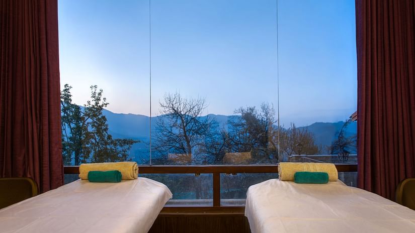 Two massage beds in a spa room with large windows  at Digantaa Resort in Mukteshwar providing a tranquil view of the mountains