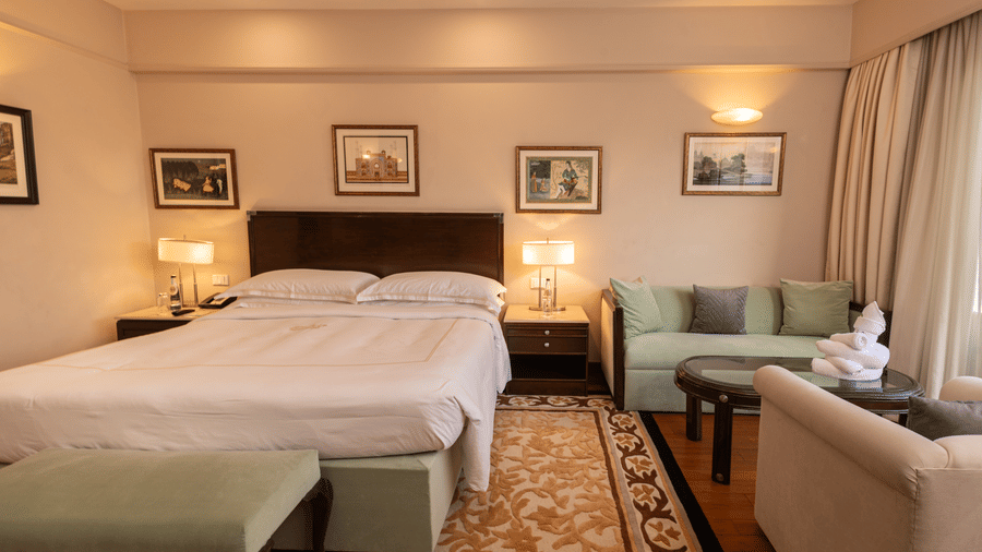 full view of out heritage balcony room with a king size bed and a family seating area with two couches placed opposite to each other - The Claridges New Delhi