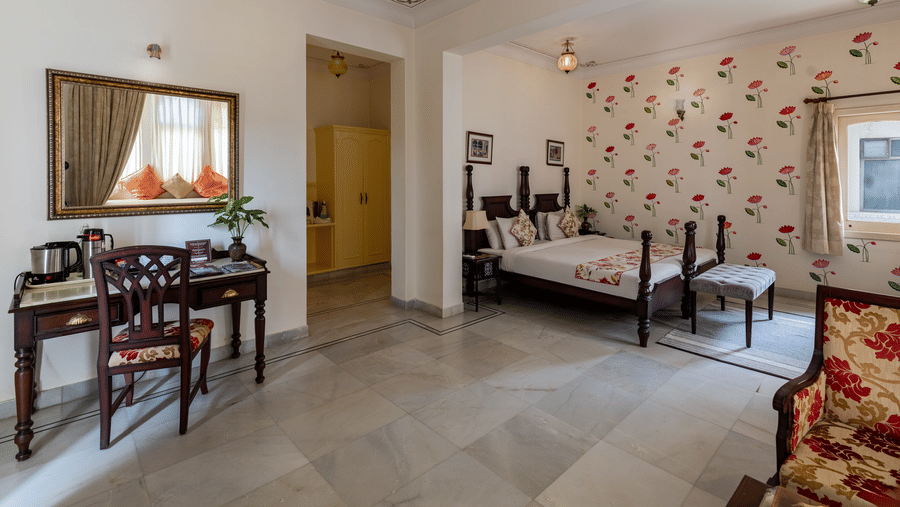 A bedroom featuring a writing desk and mirror on the left, with twin beds visible in an adjacent room area at Akshay Niwas Boutique Hotel By Amantra, Udaipur.