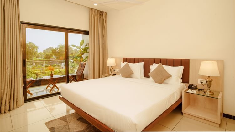 Hotel room with a large bed, side table lamps, and a view of trees outside at Arawali Ananta Elite, Jaipur.
