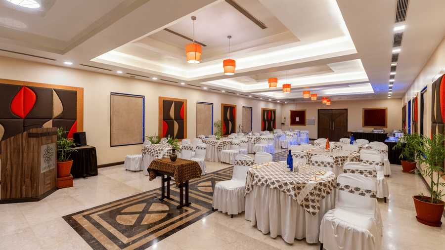 Full view of Synergy Square banquet hall in Udaipur featuring a round table setting, patterned marble flooring, and a large wall-mounted wall art - Amantra Comfort Hotel