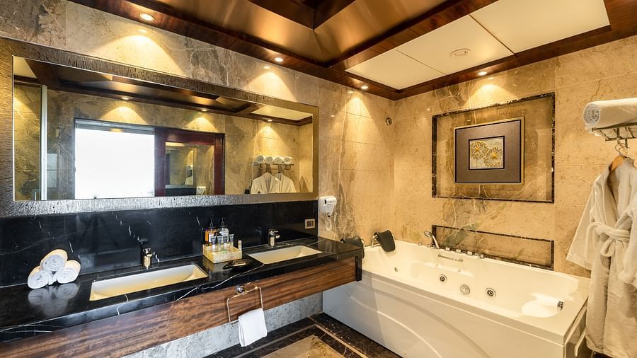 Bathroom featuring a bathtub, two wash basins, and a large mirror with toiletries neatly placed nearby, warmly lit at Crescent Spa & Resort, Indore