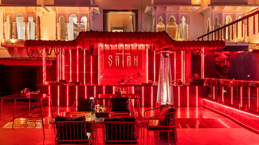 A bar with rich red light illuminating architectural features and some wooden chairs.