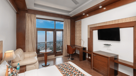 Guest room with seating area, writing desk, and television at The Solitaire Resort, featuring wooden decor and large windows for natural light and outdoor views.