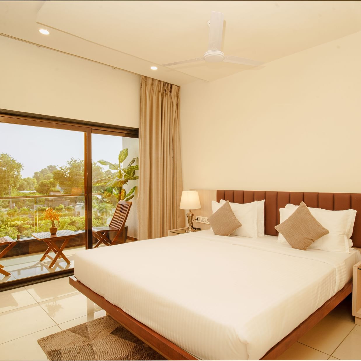 Hotel room with a large bed, side table lamps, and a view of trees outside at Arawali Ananta Elite, Jaipur.