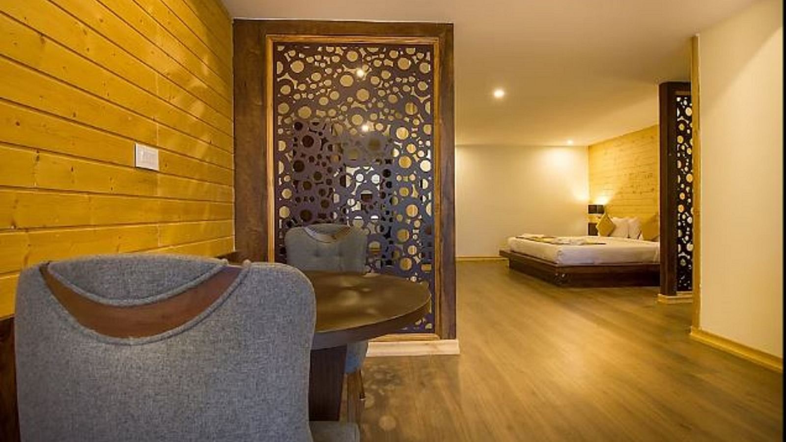 An image of a room featuring the living area with sofa set and table and the background showcasing the bed adorned with warm lighting - Yashshree Sanderling, Darjeeling