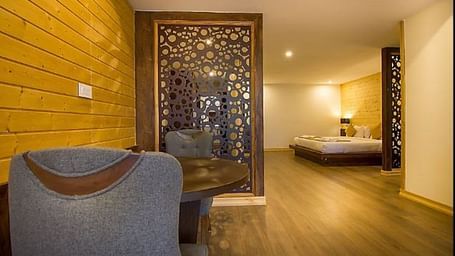 An image of a room featuring the living area with sofa set and table and the background showcasing the bed adorned with warm lighting - Yashshree Sanderling, Darjeeling