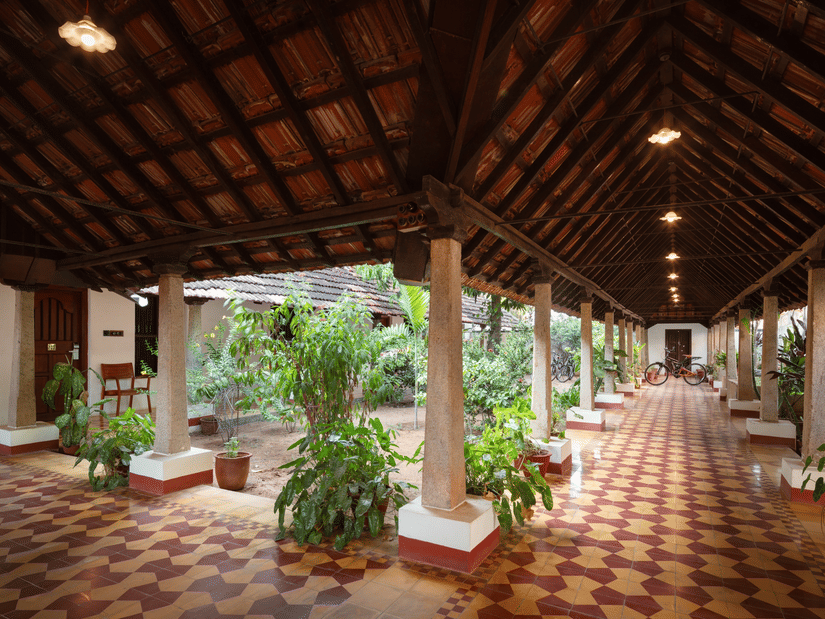 Traditional Indian courtyard at Chidambara Vilas Resort, featuring decorative floor rangolis and a distinctive wooden overhead structure - Chettinad Resort Contact