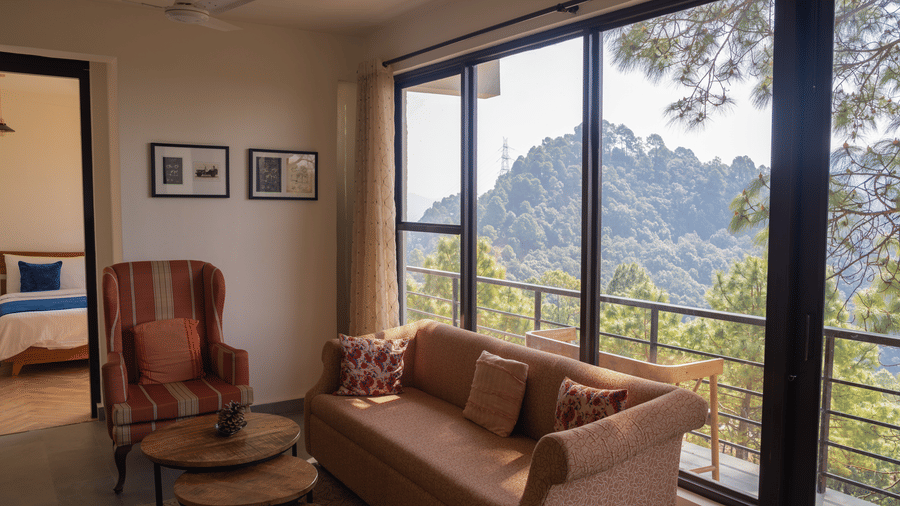 A sofa and an armchair face a coffee table inside the Pine Forest Suite. Large windows offer a view of a hill and trees.