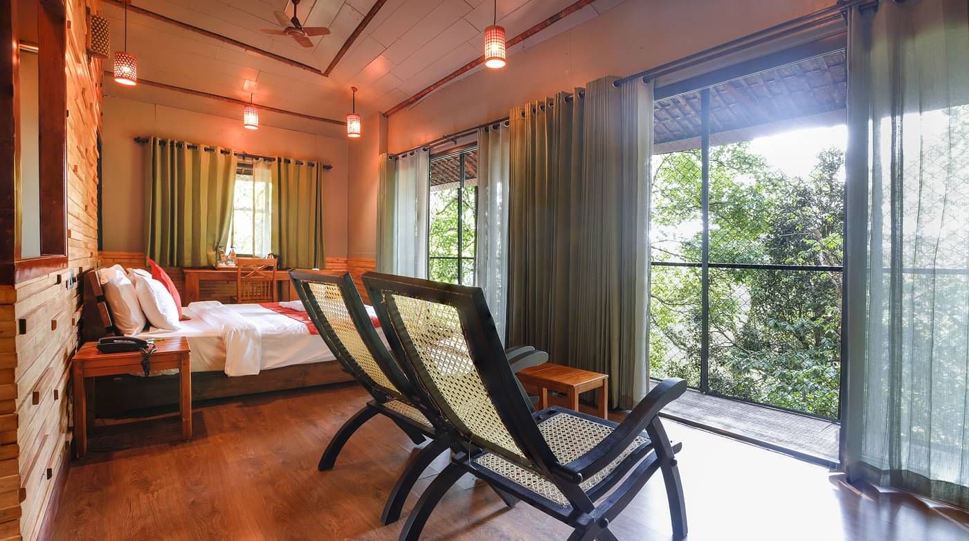 Two chairs and a bed in a room with balcony that offers forest views | Vythiri Resort. Wayanad