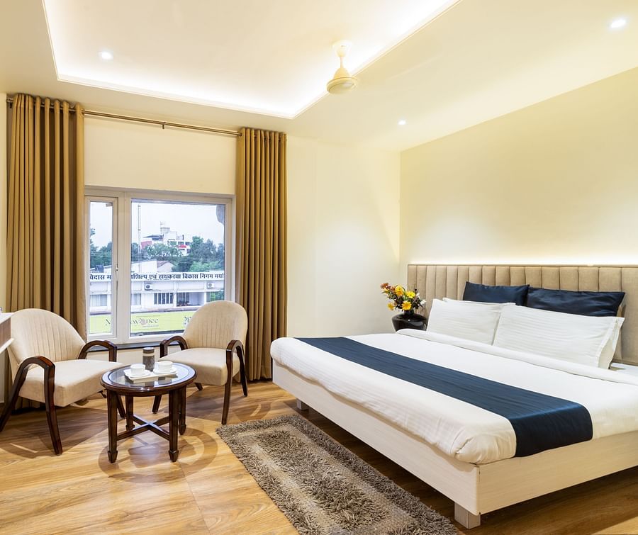 A room featuring two sofa chairs, a coffee table, a TV and a white bed - Hotel Meghdoot, Bhopal
