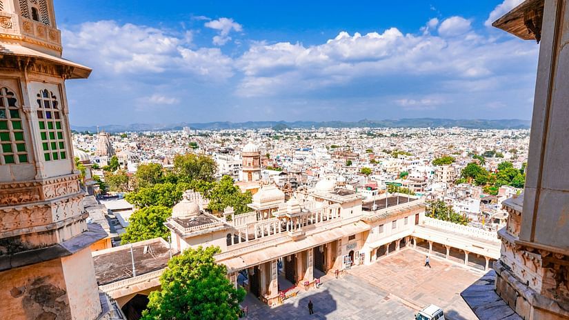 Panoramic view of Udaipur, India, from the City Palace, showcasing the city's intricate architecture, bustling streets, and surrounding hills.