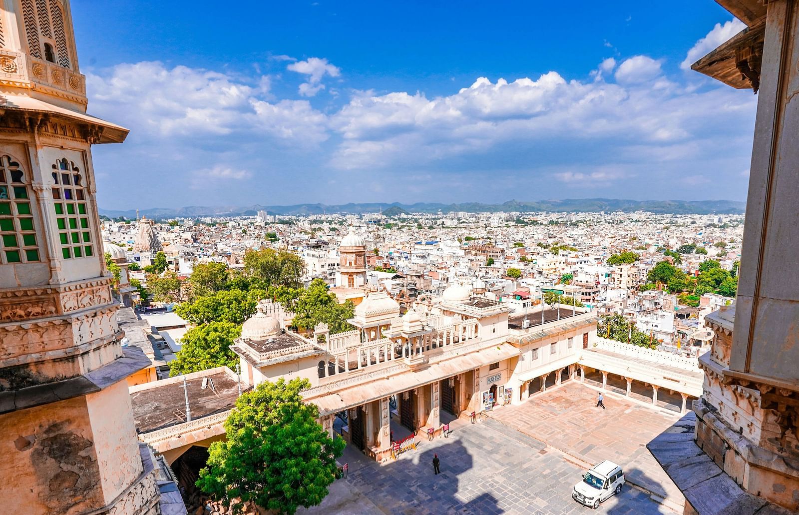 Panoramic view of Udaipur, India, from the City Palace, showcasing the city's intricate architecture, bustling streets, and surrounding hills.