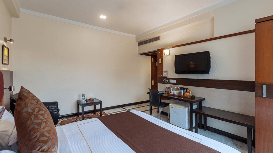 An overhead shot of the Royal Room showing a neatly made double bed facing a wall-mounted television, with warm ambient lighting and modern furnishings - Amantra Comfort Hotel