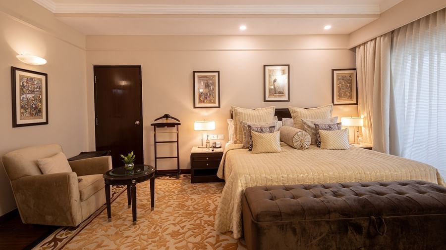 image of the bedroom of the heritage terrace room with plush bedding and a single seater beige coloured couch - image of a spacious and an elegant bedroom of the heritage terrace room - The Claridges New Delhi
