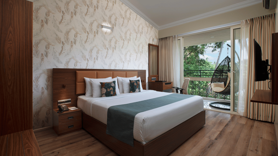 Suite with a large double bed, elegant decor, wooden flooring, and a balcony overlooking lush greenery and palm trees at Ocean Palms Goa