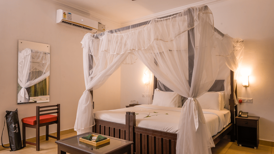 A guest bedroom at Ayur On The Beach Nattika featuring a dark wood 4-poster bed with a draped mosquito net.