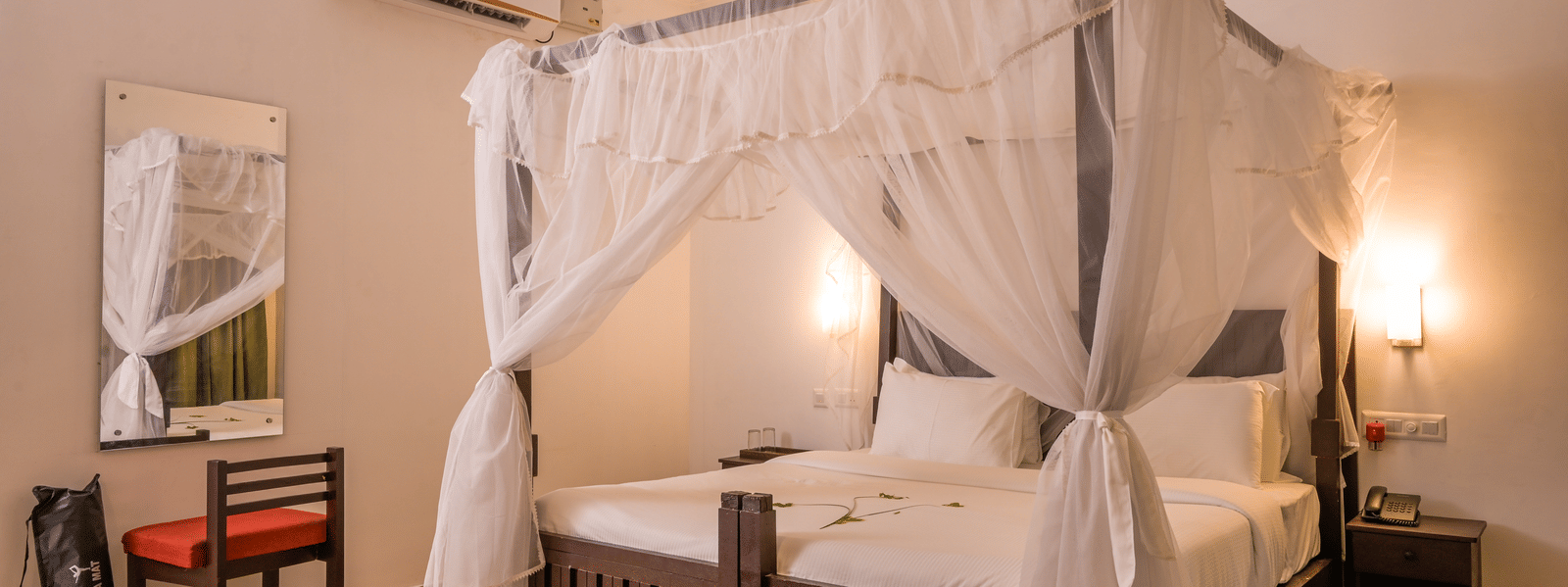 A guest bedroom at Ayur On The Beach Nattika featuring a dark wood 4-poster bed with a draped mosquito net.